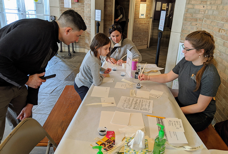 History Professor Chris Magra, his wife Elizabeth, and their daughter Colette watch as English graduate student Caitlin Branum Thrash demonstrates medieval scribal techniques at Family Medieval Day.