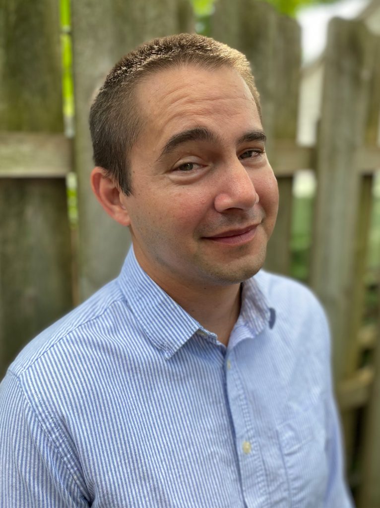 Headshot of a man with short blonde-brown hair in a blue button-up shirt