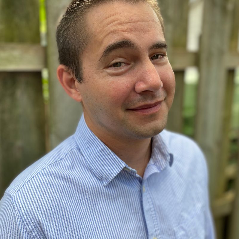 Headshot of a man with short blonde-brown hair in a blue button-up shirt